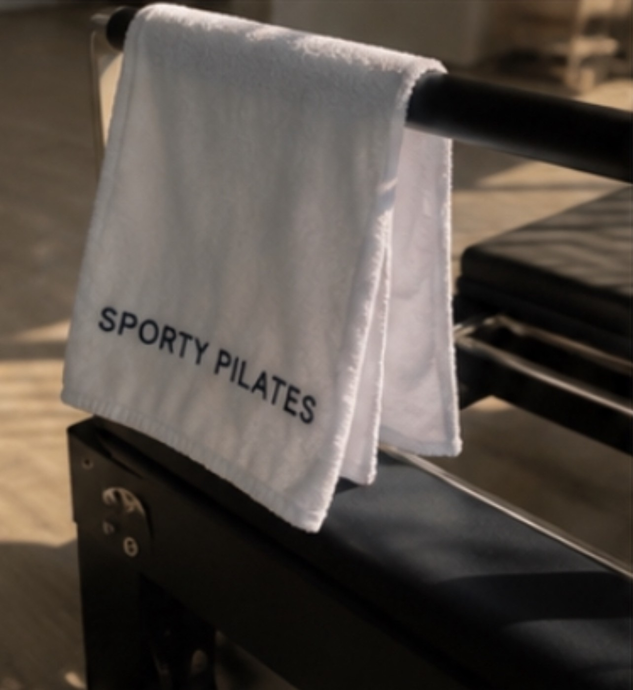 A white Sporty Pilates towel draped over a black reformer in the home studio.